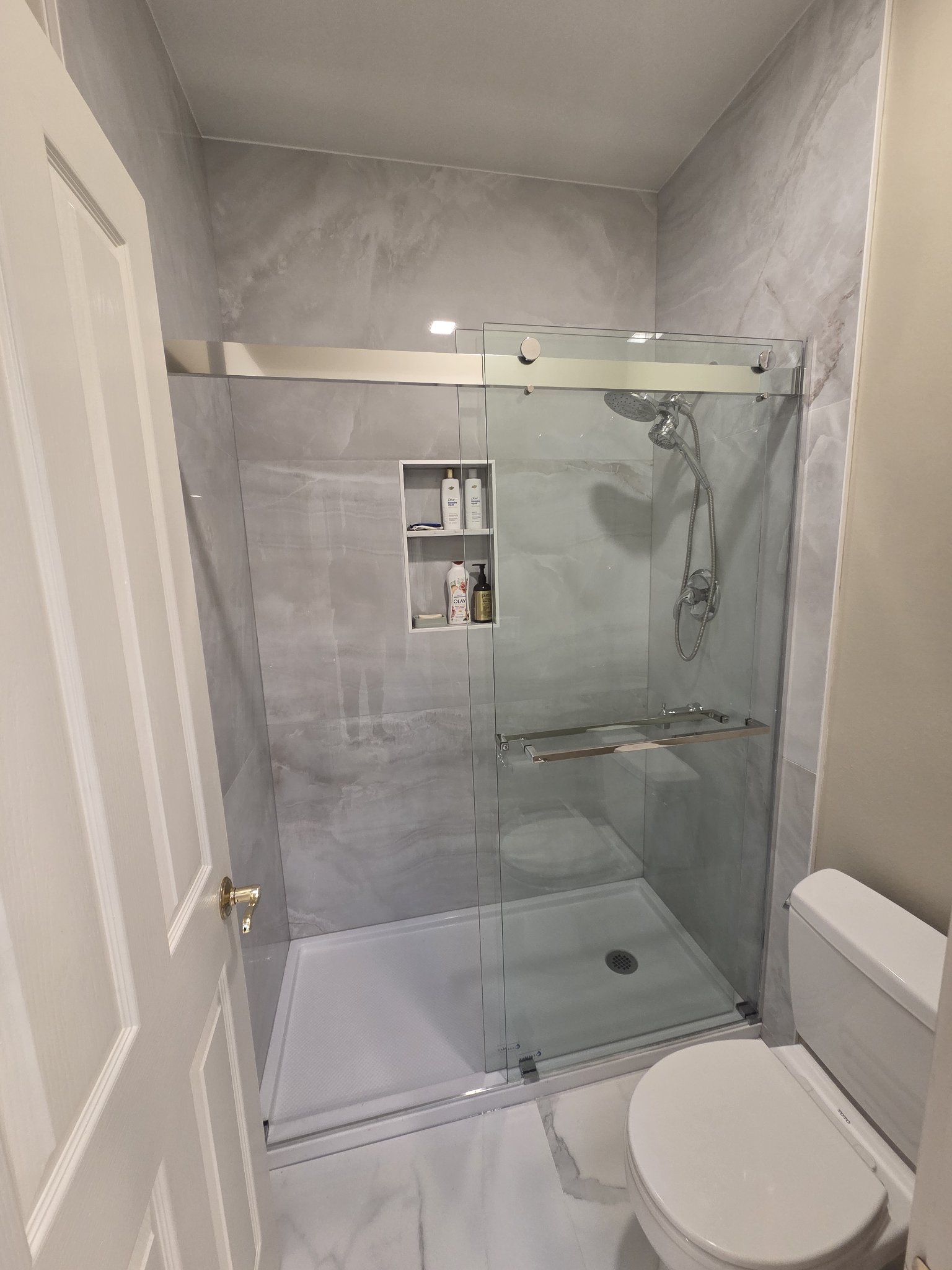 After: walk-in shower with large-format gray marble-look wall slabs, frameless glass door, and built-in shampoo niche in Renton, WA
